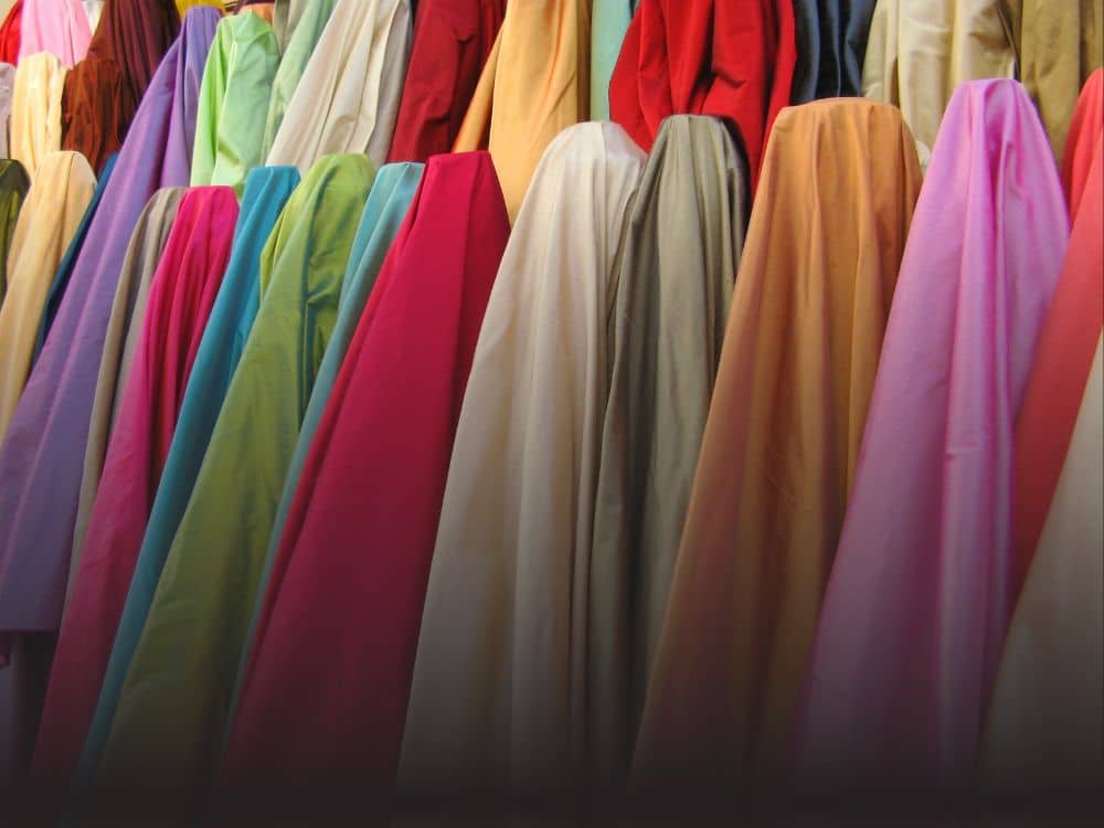 A vibrant display of colorful fabrics hanging in a row, showcasing various hues including red, green, blue, pink, and yellow, arranged in a visually appealing manner.