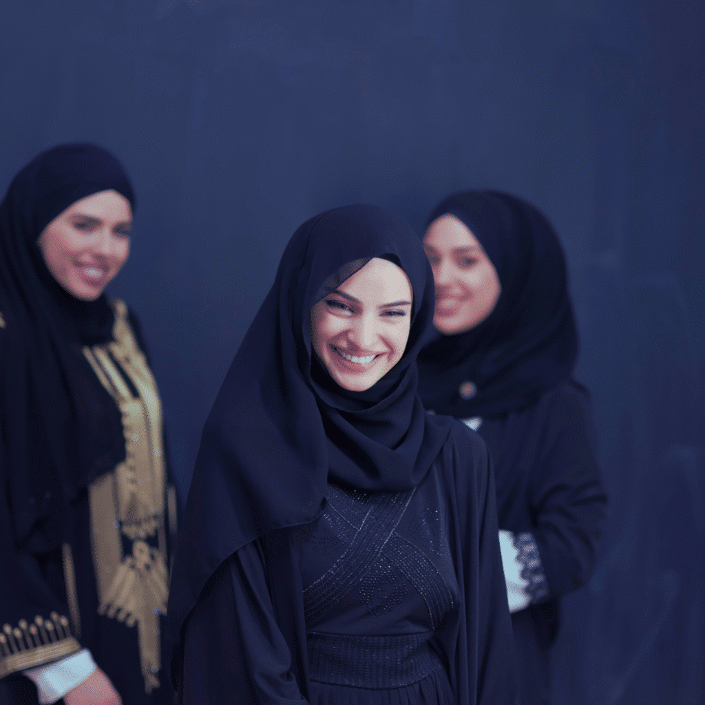 Three smiling women in elegant black abayas and hijabs – Islamic clothing wholesale fashion.