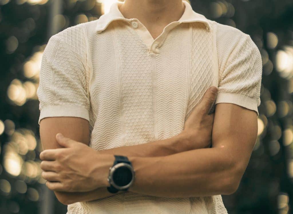 Close-up image of a man wearing a cream-colored, embroidered polo shirt, with a focus on the detailed stitching and fabric texture.