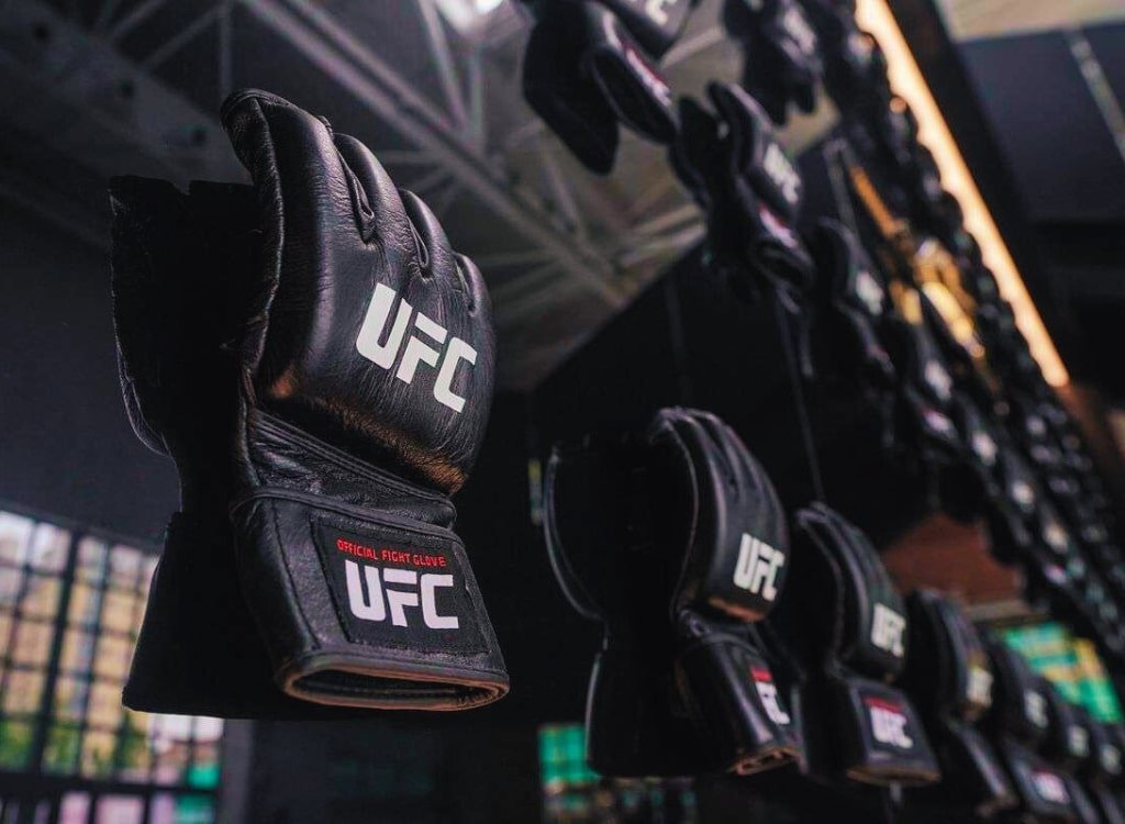 A close-up of black MMA gloves with the UFC logo hanging on display in a store or gym.