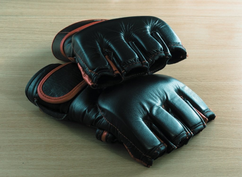 A pair of black MMA gloves with brown accents placed on a wooden surface.
