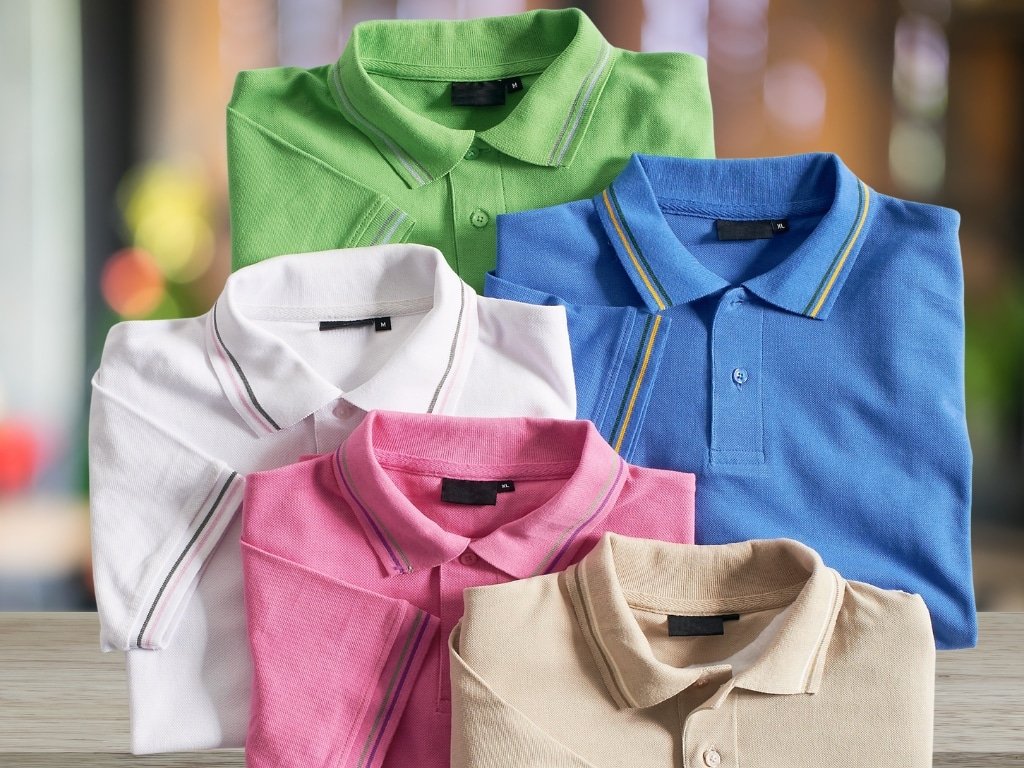 Colorful folded polo shirts in green, blue, white, pink, and beige displayed on a wooden surface.