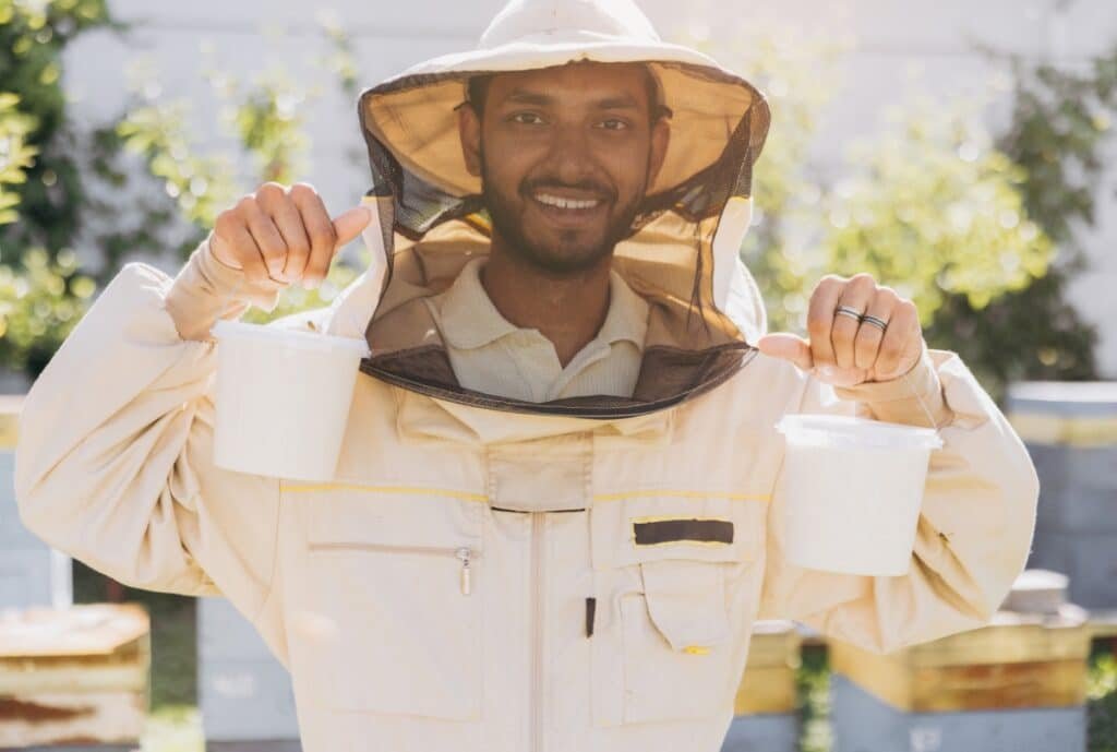 Beekeeping protective suit with veil, gloves, and radiant protective gear laid out on a wooden table.