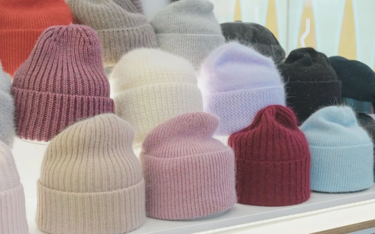 A display of colorful knitted beanies on a white shelf.